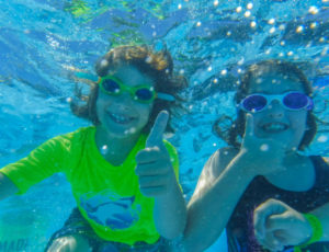 two campers underwater with their thumbs up