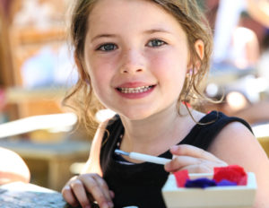 a young girl smiling with a paint brush