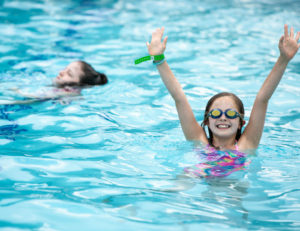 a girl in the water with goggles on and her hands up