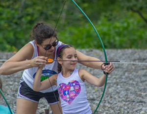 a counselor helping a girl aim her bow and arrow