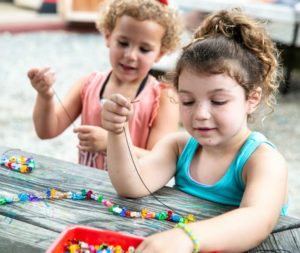 two young girls making necklaces