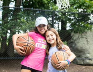 two girls together holding basketballs