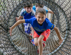 a close up of a boy who is climbing through a netted tunnel