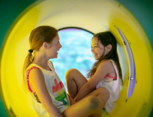 two girls laughing and hiding in a play tunnel