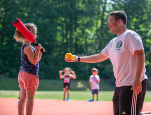 A counselor holding a softball for a girl to hit