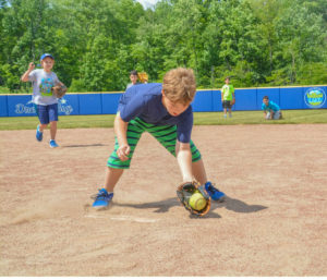 A boy picking up a softball with a mitt