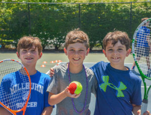 three boys smiling holding tennis rackets and a tennis ball