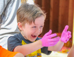 a boy laughing with pink paint on his hands